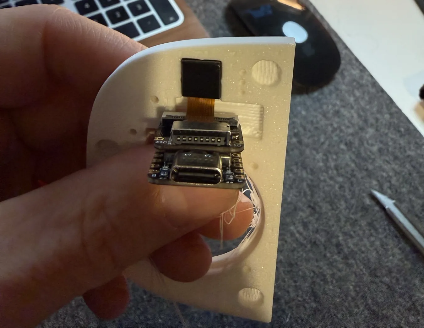 The XIAO board and its camera held against the back of a printed face plate