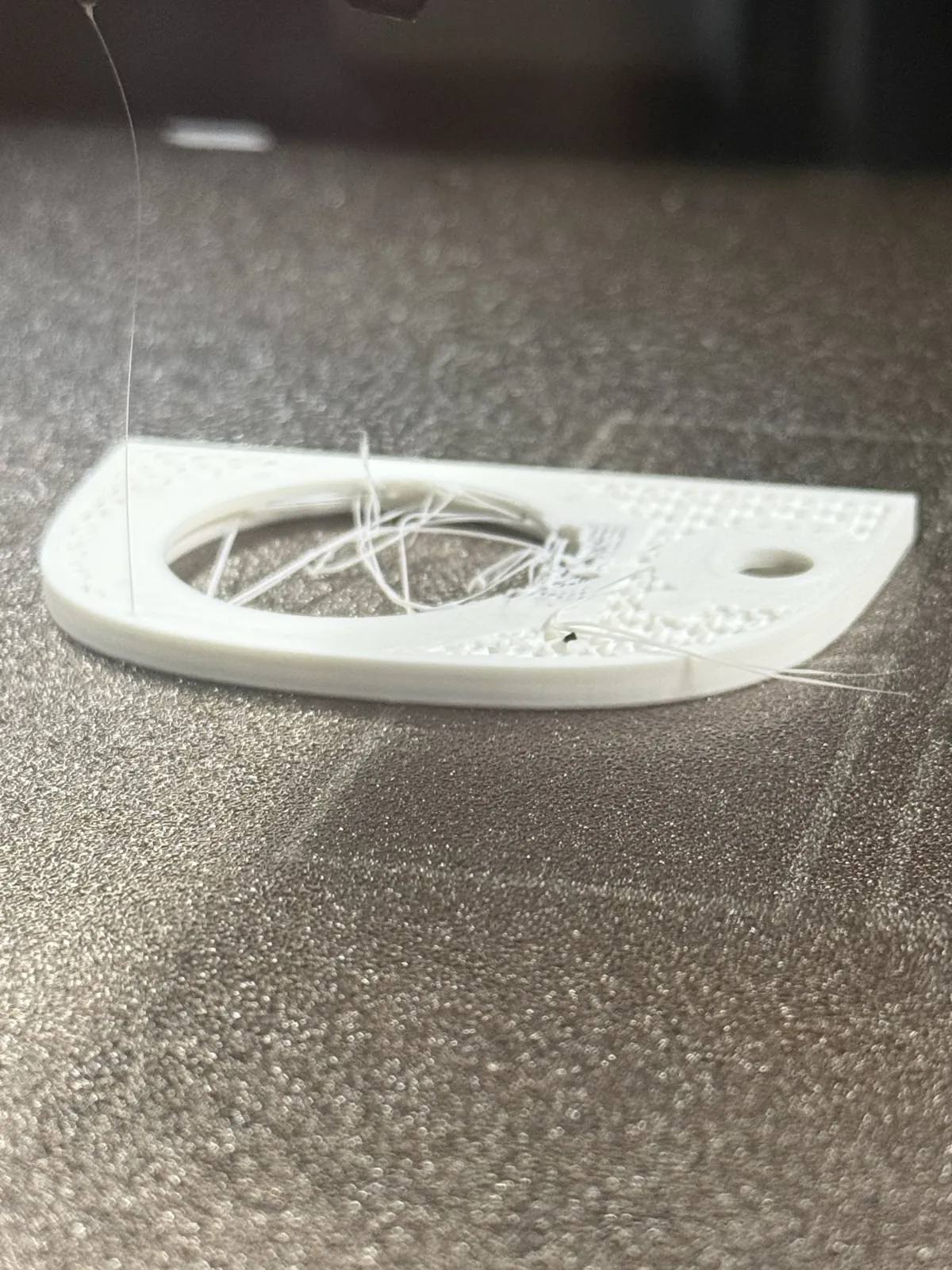 A white face plate on the print bed with loose strings of filament round its round window
